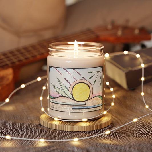 A lit candle in a clear glass jar sits on a round wooden coaster, surrounded by warm fairy lights. The jar has a cream-colored label with a colorful illustration of a yellow sun, green leaves, and pink lines, with a blurred guitar and book in the background.