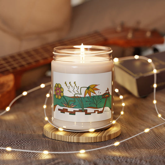 A lit candle in a clear glass jar sits on a round wooden coaster, surrounded by warm fairy lights. The jar has a white label with a colorful botanical illustration.